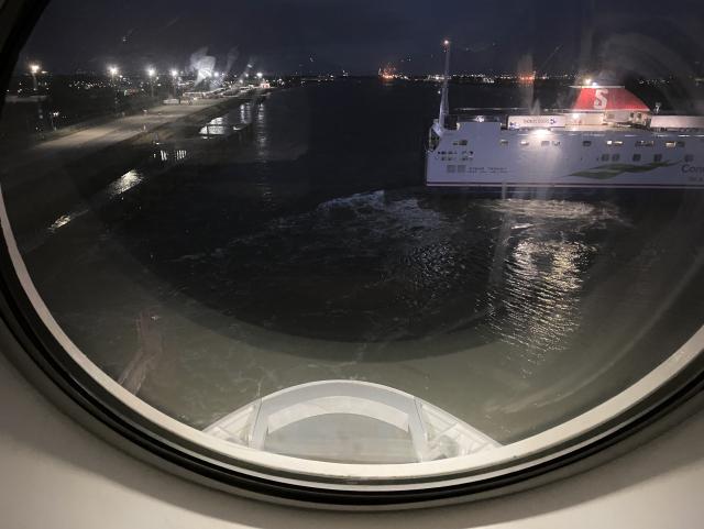 View out of a round window onto dark waters. Below you can see the bow of the ship.