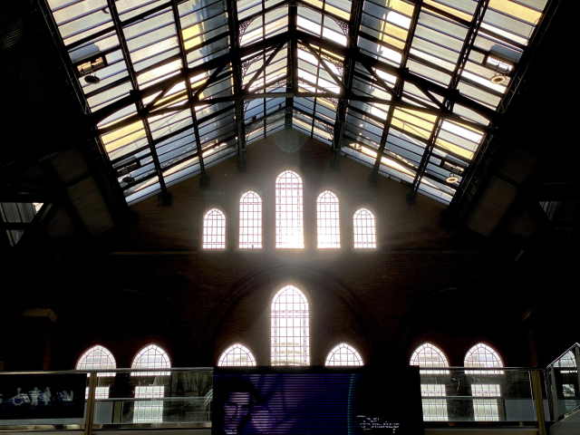 The gable of the station hall. The sun backlights the tall, arched windows and the coloured glass ceiling.