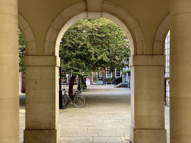 View through a sandstone arch into a courtyard with trees and a parked bicycle.