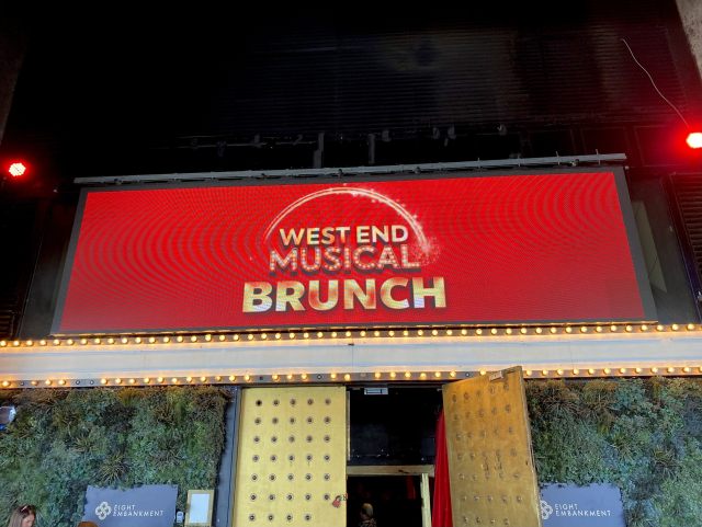 An sparkly electronic banner over a door reading “West End Musical BRUNCH.”