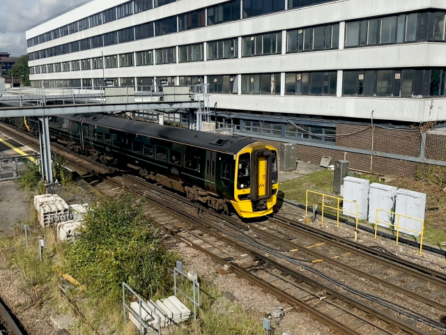 Shot from left above of a train leaving a station. The train is (very) dark green GWR class 166 diesel with a yellow front.