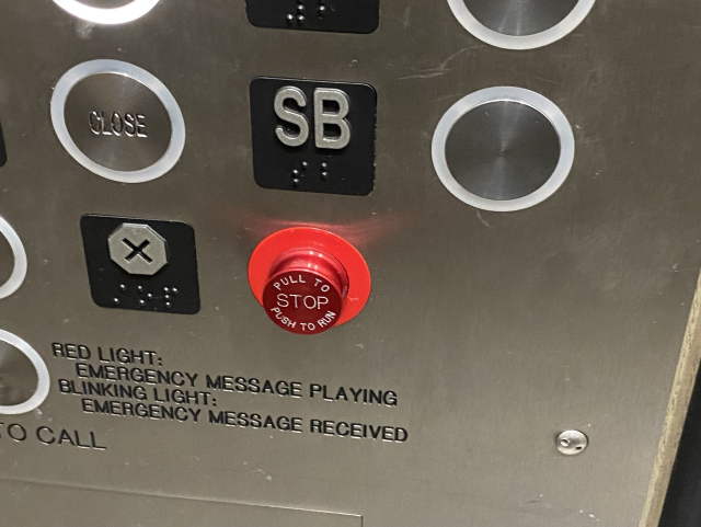 The control panel of a lift. There is a red button labelled “Pull to stop, push to run.”