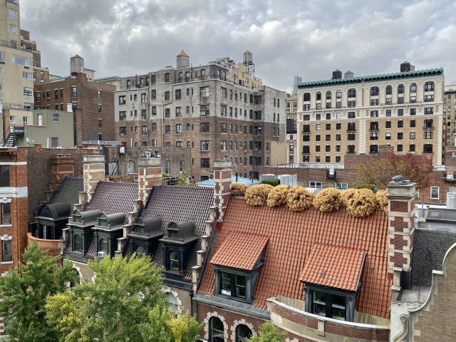 View over the roofs of a row of town houses with taller red, white, and yellow brick buildings looming beyond.