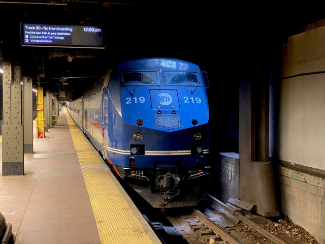 The front of MTA blue Genesis diesel locomotive number 219 at an underground platform. The platform indicator reads “Track 30. No train boarding. 12:00 p.m.” 