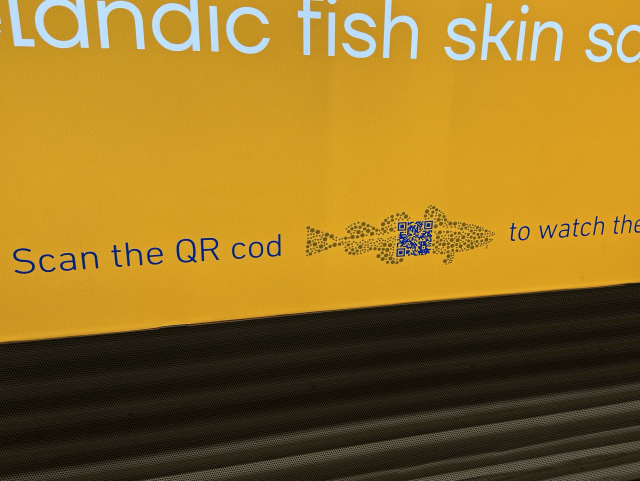 A yellow sign displaying the phrase "Scan the QR cod" alongside a QR code in an illustration of fish. It’s a pun, you see.