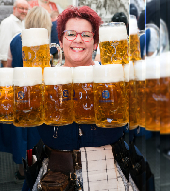 Bedienungen im Löwenbräu im Oktoberfestzelt. Frau lacht und hat viele Maß Bier in der Hand. 