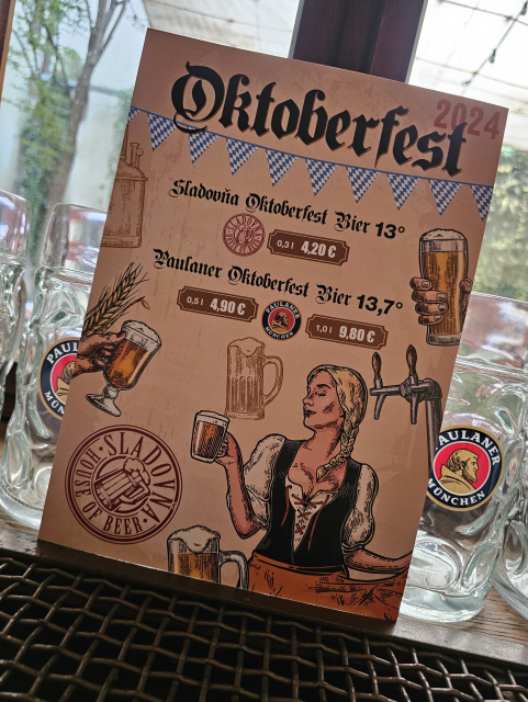 leták/plagát na Októberfest pivo Paulaner a Sladovňa... vo vitríne okna v pozadí litrové poháre Paulaner