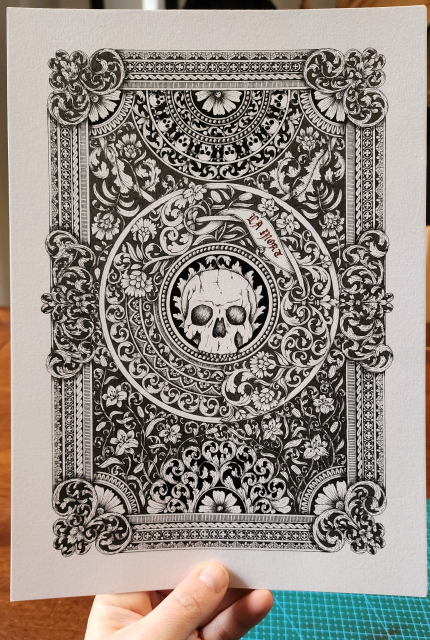 A hand-drawn black ink artwork of a skull surrounded by detailed, ornate decorations of swirling acanthus leaves, lily flowers, a banner that reads 'LA MORT' in red ink blackletter script, and ornaments in with swirling acanthus leaves and flowers in the corners. It's very detailed and intricate.