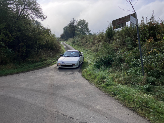 Weißes Auto biegt auf einem Feldweg an einer Kreuzung mit eingeschaltetem Blinker rechts ab.