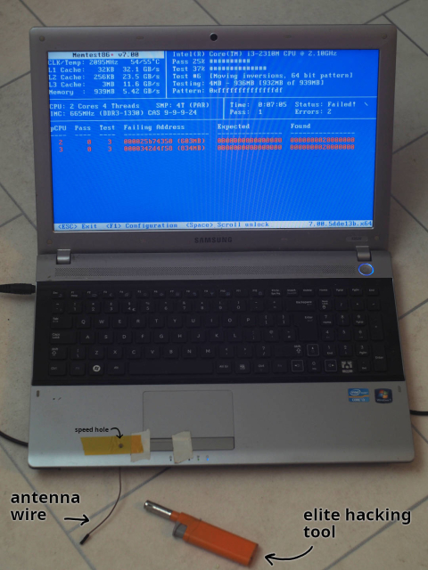 a laptop running memtest86+, showing two errors. a wire pokes out from the lower edge of the laptop, annotated as "antenna wire". an orange cigarette/barbecue lighter sits next to it, annotated as "elite hacking tool"