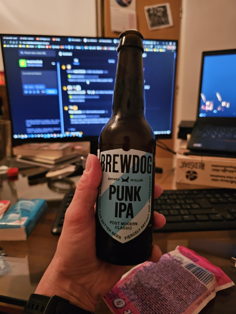 mnou držiac flaškové pivo v Brewdog Punk IPA v pozadí izba