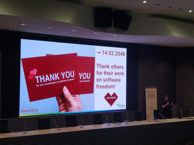 slide with "Thank you for your contribution to software freedom" and red hearts. person with mic next to it.