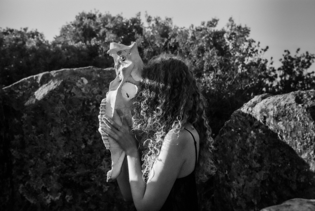 Portrait. BW picture of a girl holding a horse skull against her face. The girl's face is non visible. She's in the middle of a dolmen circle. 