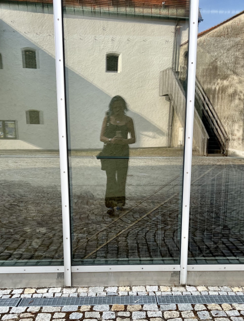 Window-Selfie of me, a non-binary person, on a sunny day. You can't really identify me clearly, but I am a slim, tall person with slim arms (they were always very "feminine"). I wear a spaghetti-string-strap black top and what looks like some black pair of pants.

Since you can't make out the face very clearly, this could in fact 100% be my daughter.