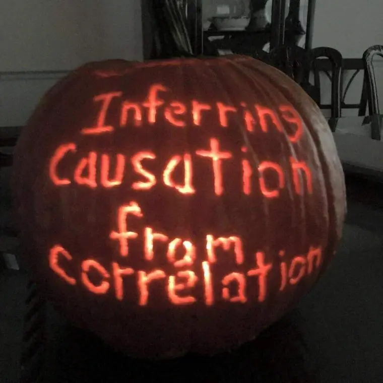 A photograph of a flaming Halloween pumpkin engraved with the words "Inferring causation from correlation"