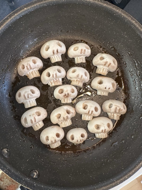 Mushrooms shaped like skulls are frying in a pan with some oil.