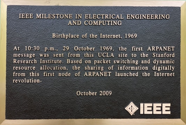 A black commemorative plaque with gold frame, inscribed with gold letters. It reads:

"At 10:30 p.m., 29 October 1969, the first ARPANET message was sent from this UCLA site to the Stanford Research Institute. Based on packet switching and dynamic resource allocation, the sharing of information digitally from this first node of ARPANET launched the Internet revolution."