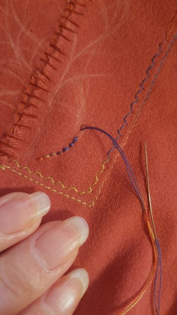 A very close up of the embroidery going on top of the patch, on the right side. The edges of the tear have been overlapped and loosely stitched together with a red linen thread, that is the wrong thickness, but roughly the right colour. The embroidery is a stem or vane in progress, done in teeny tiny little backstitch. There are varying lines of possible directions for the line of stitching to go, Sini has not been able to decide and has sketched right on top of the fabric.