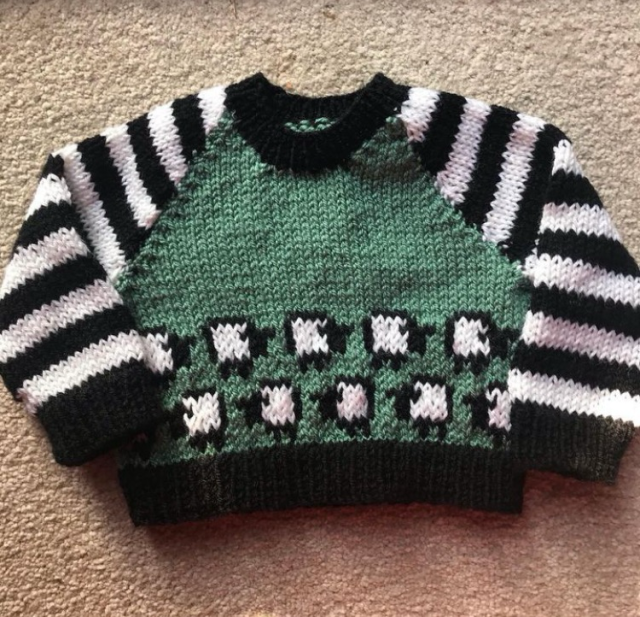 Hand knitted baby jumper with a green body populated by sheep, with black and white striped raglan sleeves (I obviously didn’t have much wool of each colour!)