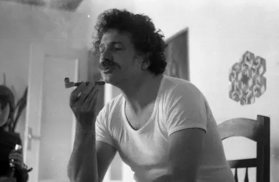 Ricardo Pachón en su casa, en 1976, camiseta interior blanca, pelo rizado y bigote, fumando de una pequeña pipa de las que se usan no para tabaco precisamente, sino para hachís o marihuana. Su gesto es de fruición y deleite. Vamos, que se lo está pasando pipa. Archivo flamenco, 1976.