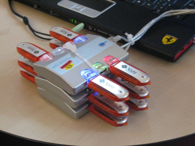 Photo showing a three USB hubs zip tied together with 12 Sun USB thumb drives attached to the 3 hubs. A laptop can be seen nearby where it's plugged into.