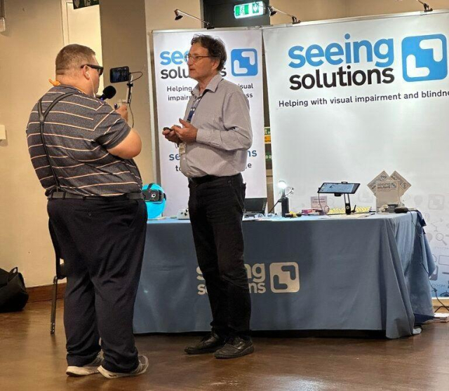 Tim interviewing Philip Ward of Seeing.Solutions at Sight Village Leeds 2024. Tim is holing a gimbal with his iPhone recording Philip and a Microphone in Tim's other hand.