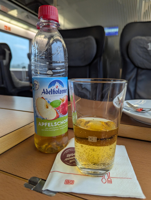 A photo of Mehrweg PET bottle and a DB branded glass half full with yellowy liquid.