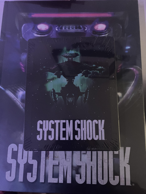 The System Shock remake steel case placed on top of the Art of System Shock hardcover book