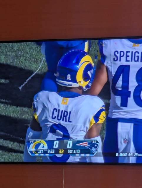 A football player wearing a jersey with the last name "CURL" displayed on the back, standing on a football field. The image is shown on a TV screen.