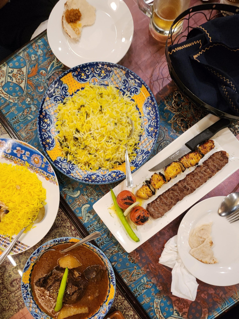 Plates of basmati rice, skewered meats, and stewed lamb on a table