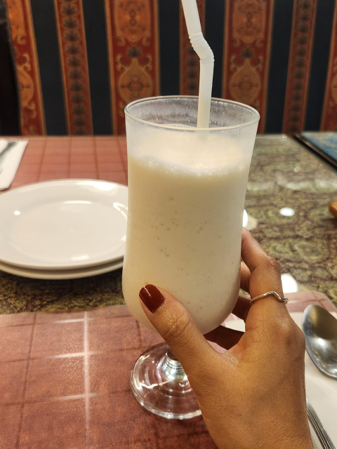 A hand holding a glass of yogurt shake with straw