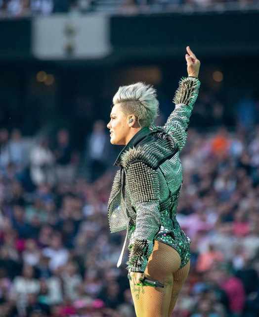 P!nk, in fishnets and a mirrorball bodysuit under a leather jacket just unbelievably covered in spikes, with her side-shave and kinda mowhawky blonde hair, on stage and raising a middle finger in the air