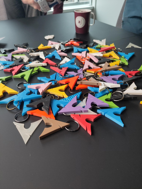 The picture shows a lot of 3d printed Arch Logo as keychain things in various colors on a meeting table.