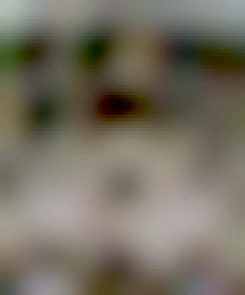 picture of a man at desk that's full of open books and notes, with more books all over the floor, and on surrounding cabinets