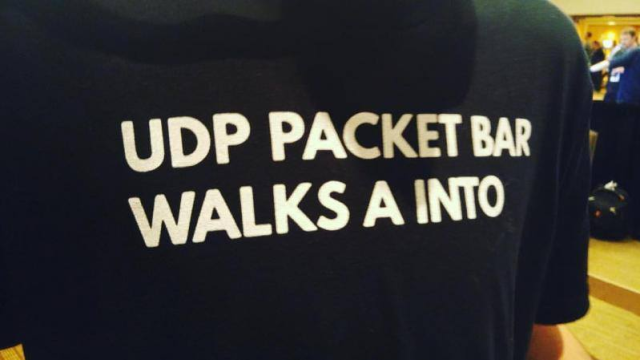 Photo of a black T-shirt, no clear surroundings are visible.

The text on the shirt reads "UDP PACKET BAR WALKS A INTO"