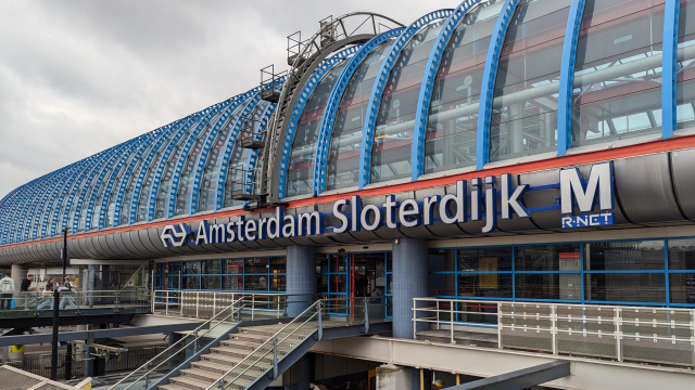 A view of an overground metro station with a big sign showing:
<NS logo> Amsterdam Sloterdijk <big letter M with smaller R-NET below it>