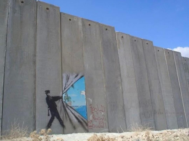 Banksy mural on the separation wall in the West Bank, Palestine, showing a stencil of a uniformed figure pulling back the concrete barrier like a curtain to reveal a vibrant tropical beach scene. The stark contrast between the oppressive gray wall and the serene imagery symbolizes hope and resistance. Arabic graffiti near the base emphasizes the local cultural and political context of the artwork.