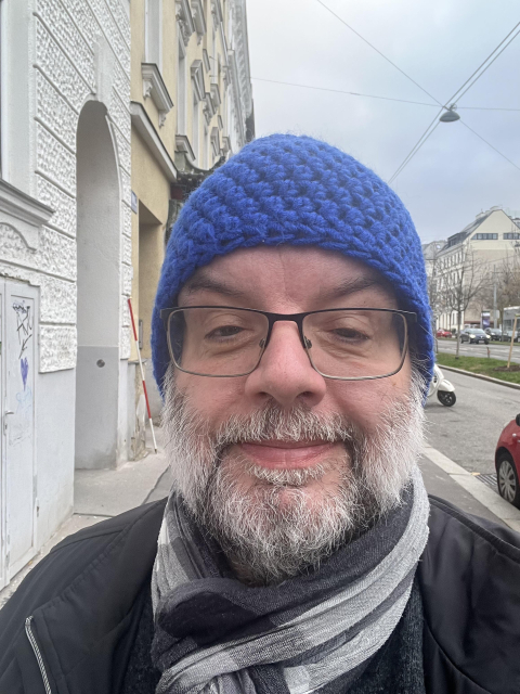 Selfie. Robert auf der Straße mit blauer Haube. Er lächelt. 