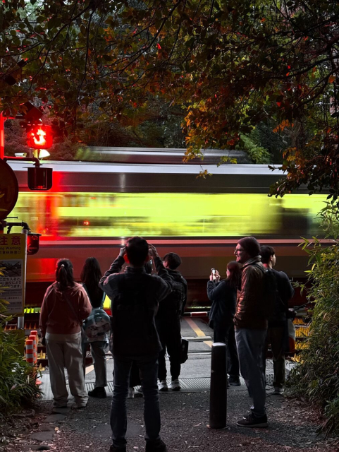 A night time view of a train crossing in Arashiyama, Kyoto. People watching a blurred and illuminated train pass by.