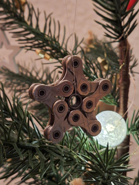 Eine Weihnachtsbaumschmuck.
Eine Fahrradkette als 5 zackiger Stern geformt. Gehängt an einem Nadelbaum.