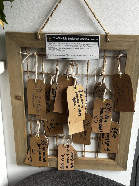 A display of hand written tags with descriptions of money off from types of books, e.g. £10 for a braw kids book. 

Sign reads, “Need a bit of help to buy a book? Take a tag and present it at the counter - no questions asked. It's that simple.
Want to pay for a tag to help someone else? Ask at the counter. Thank you.”