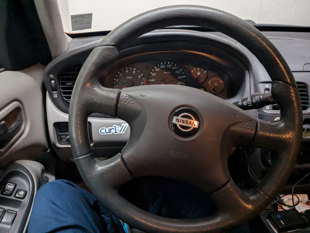 Shot from the driver seat towards the steering wheel and the dashboard of a standing car. Through the wheel's spokes a curl sticker is visible.