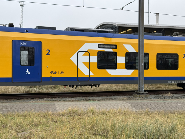 Photo of the side of a yellow and blue train with a bug white NS logo – an ICNG-B. Between the entrance door and the first window sits a smaller door without a window.