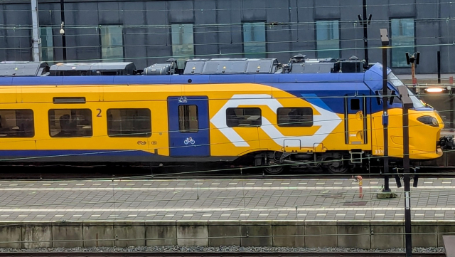 A side view of the ICING-B train in the NS flow livery. Next to the entrance door, there are tiny logos of NS and NMBS/SNCB.