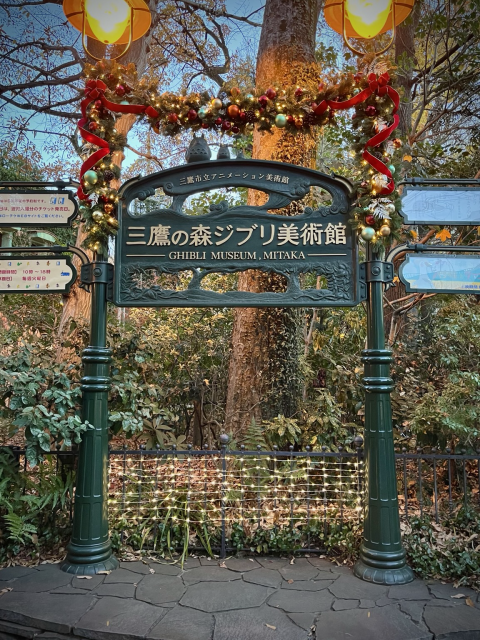 Ghibli Museum entry sign in front of thick vegetation and trees