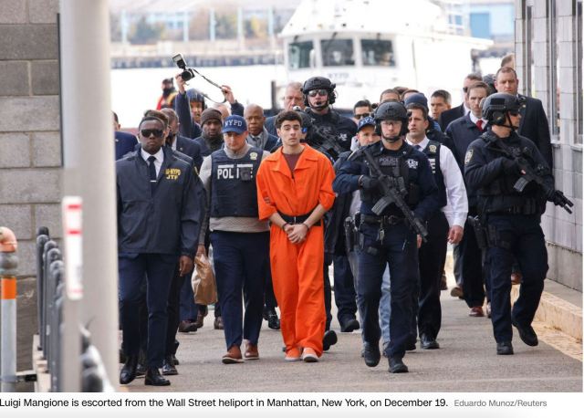 Luigi Mangione, in orange inmate clothes, hands cuffed in front of him, is marched in the streets of New York with a HUGE detail of armed pigs from the FBI and NYPD.  They carry assault rifles and wear helmets and tac gear.