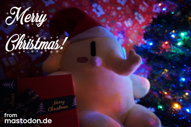 An image of a Mastodon plushie with a Christmas hat, Christmas wrapping background, presents to the left saying “Merry Christmas”, and a Christmas tree with colorful lights to the right. A text is written above and below the image on its leftward side saying “Merry Christmas! from mastodon.de”

The plushie's name is “Oskar”.