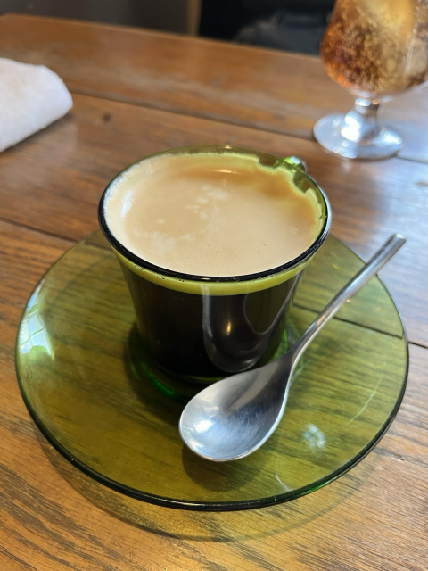 Coffee with foam in a green glass mug and a metal spoon