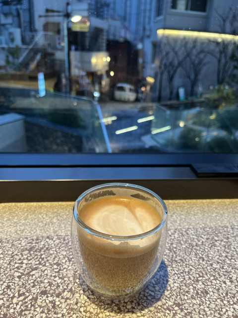 Cappuccino in a glass in front of a window with neon reflections during a rainy evening 