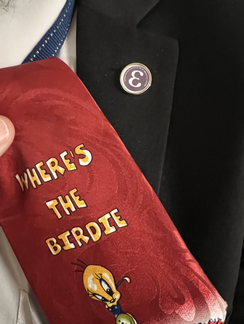 Cravate rouge avec Titi et un drôle de pin avec la lettre grecque Epsilon.